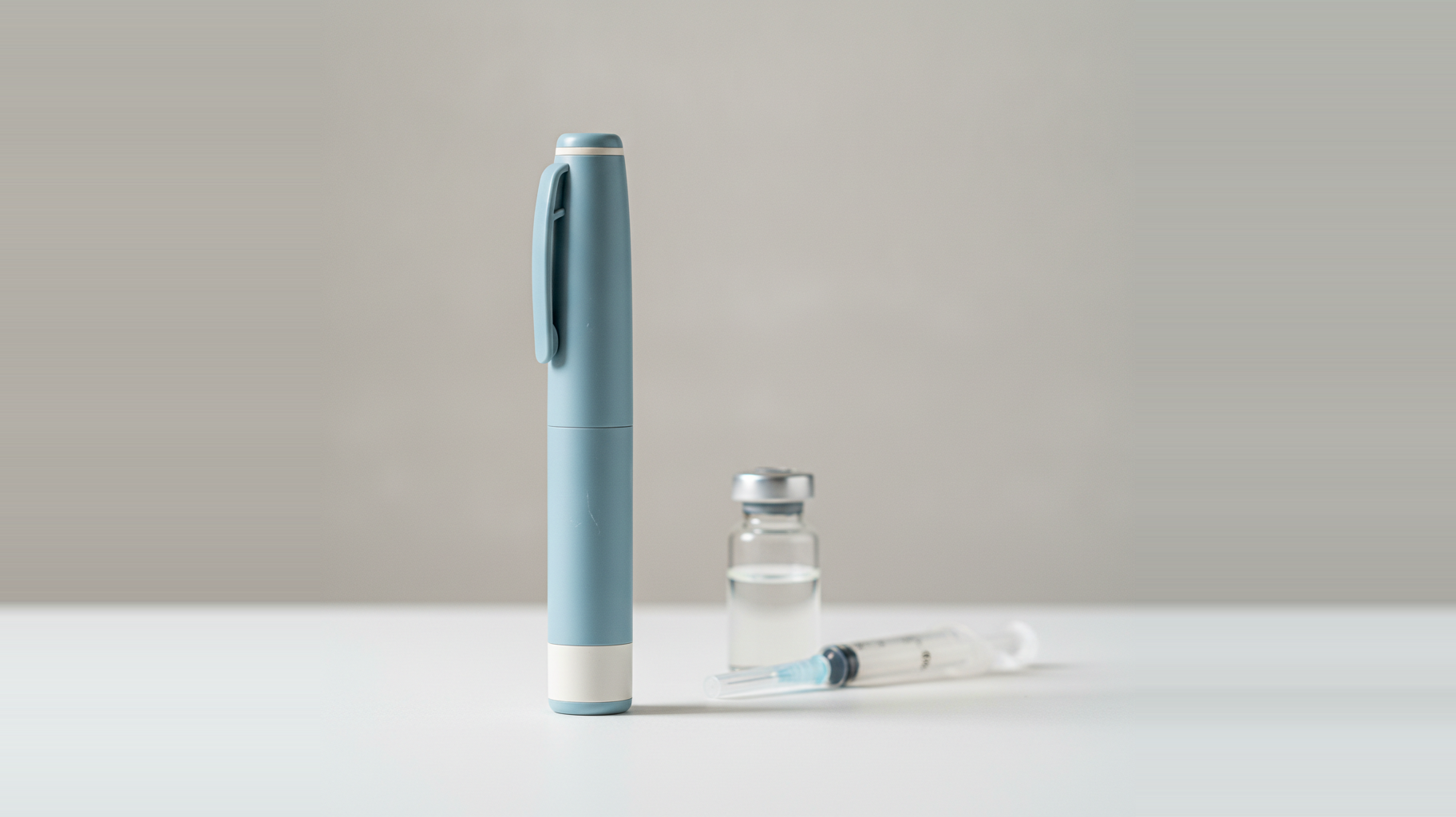 A GLP-1 injection pen standing beside a glass vial and a syringe on a clean surface — representing the semaglutide and tirzepatide products at the center of the 2024–2026 compounding and regulatory changes.